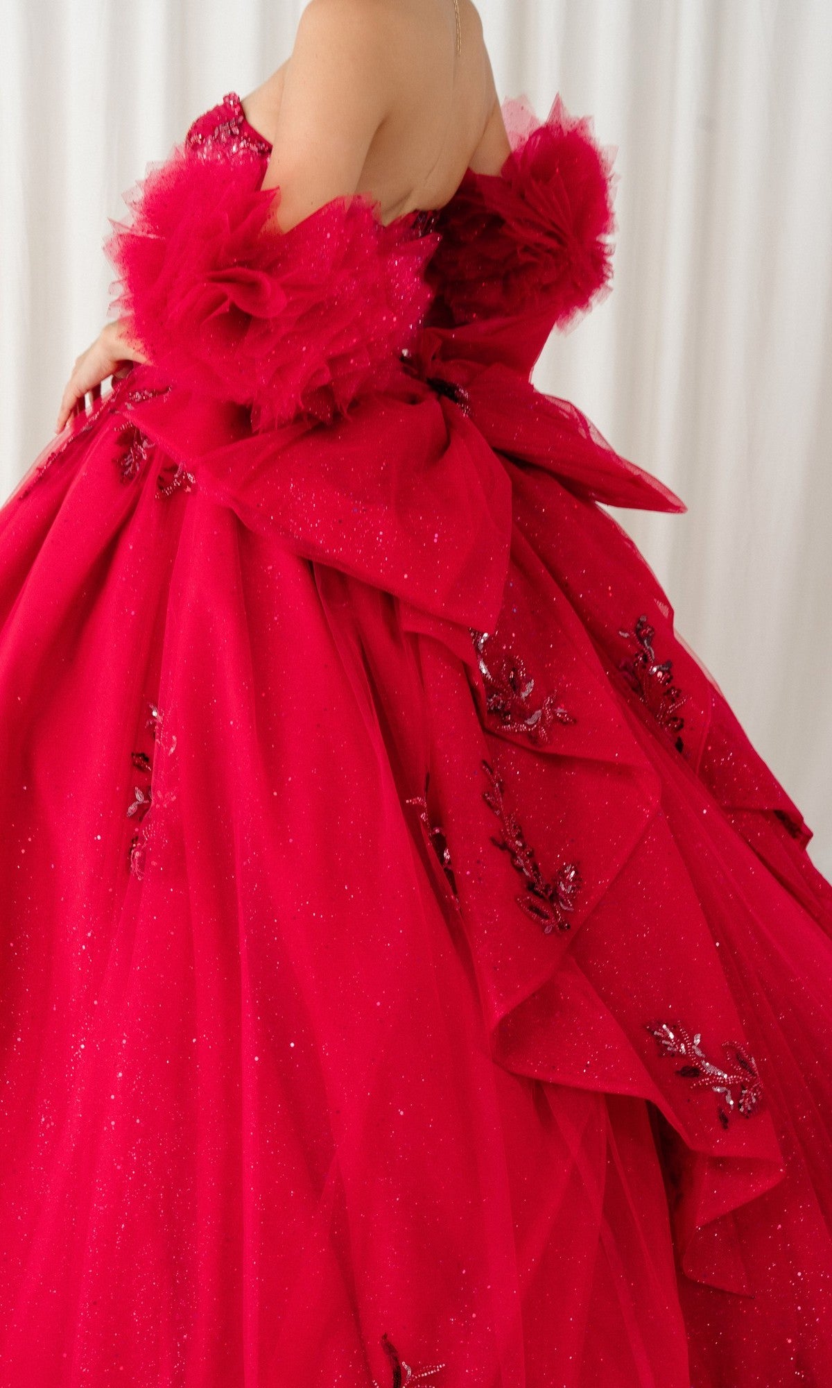A person wears the Quinceanera Dress 8380J by Cinderella Couture, a strapless ball gown featuring large bows, floral accents, and glittery tulle fabric, set against a white background.